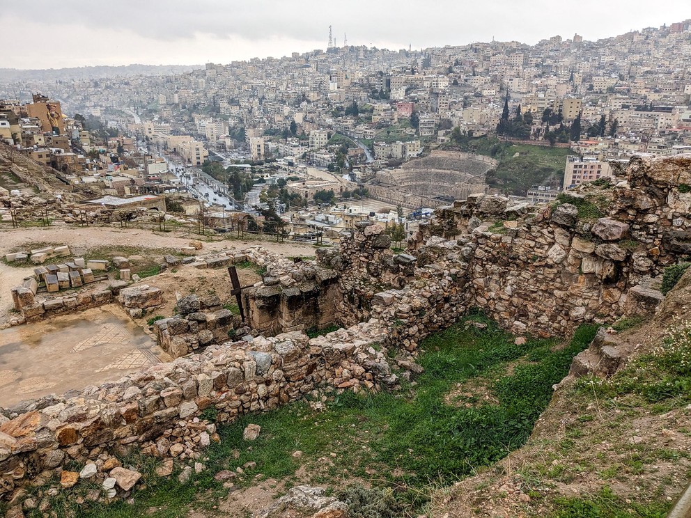 you are looking down over the ruins of the Citadel to a Roman theater carved into the hillside among white apartment buildings in historic Amman, Jordan