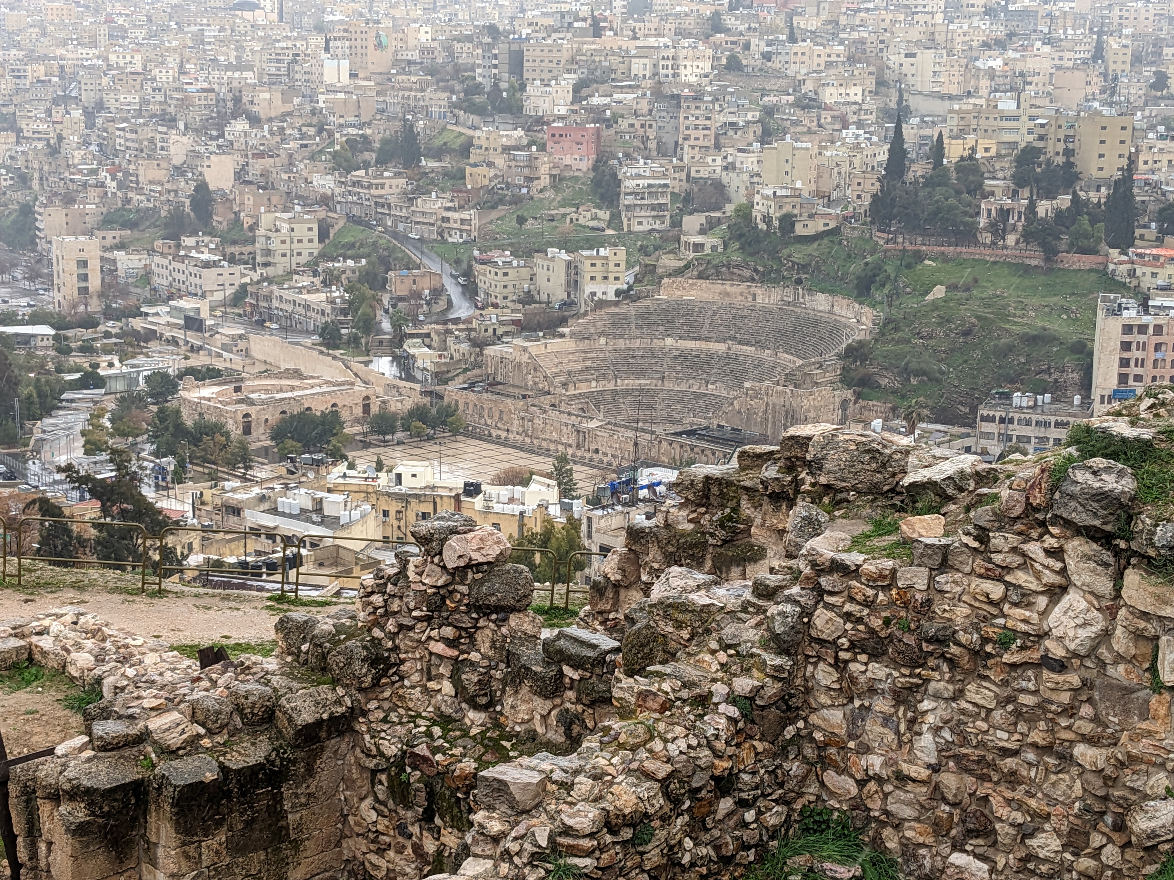 an ancient roman theater is carved into a hillside among white apartment buildings in historic Amman, Jodran
