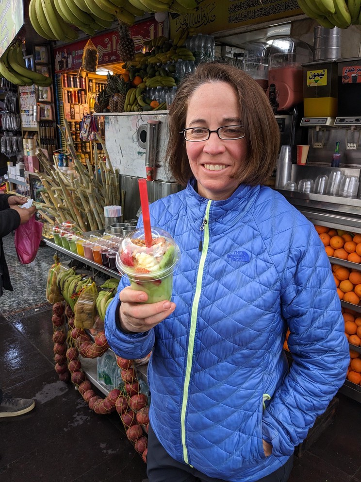 a woman smiles holding a fruit smoothie with avocados