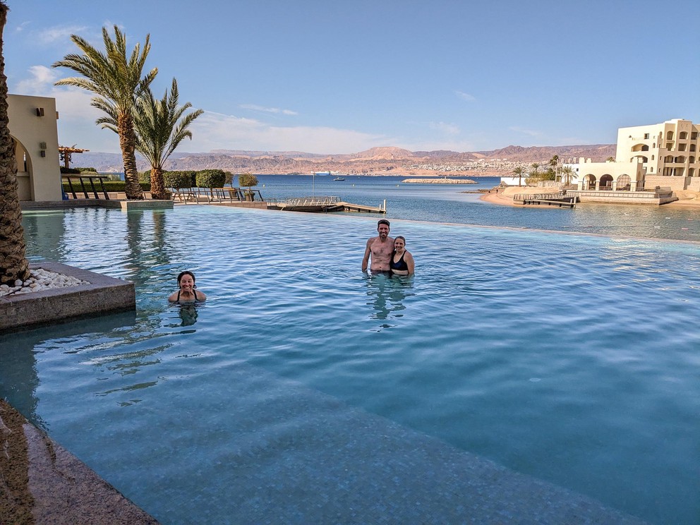 people swim in an infinity pool with views across the Gulf of Aqaba behind them