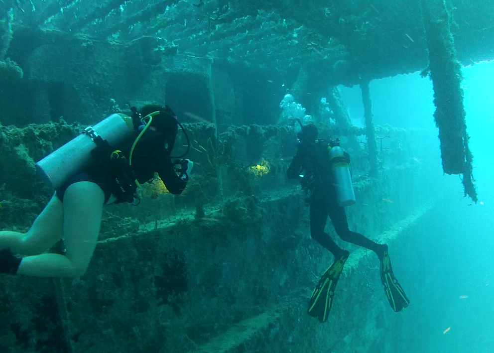 two scuba divers swim under the amphibious transport ramps of the USS Spiegel Grove