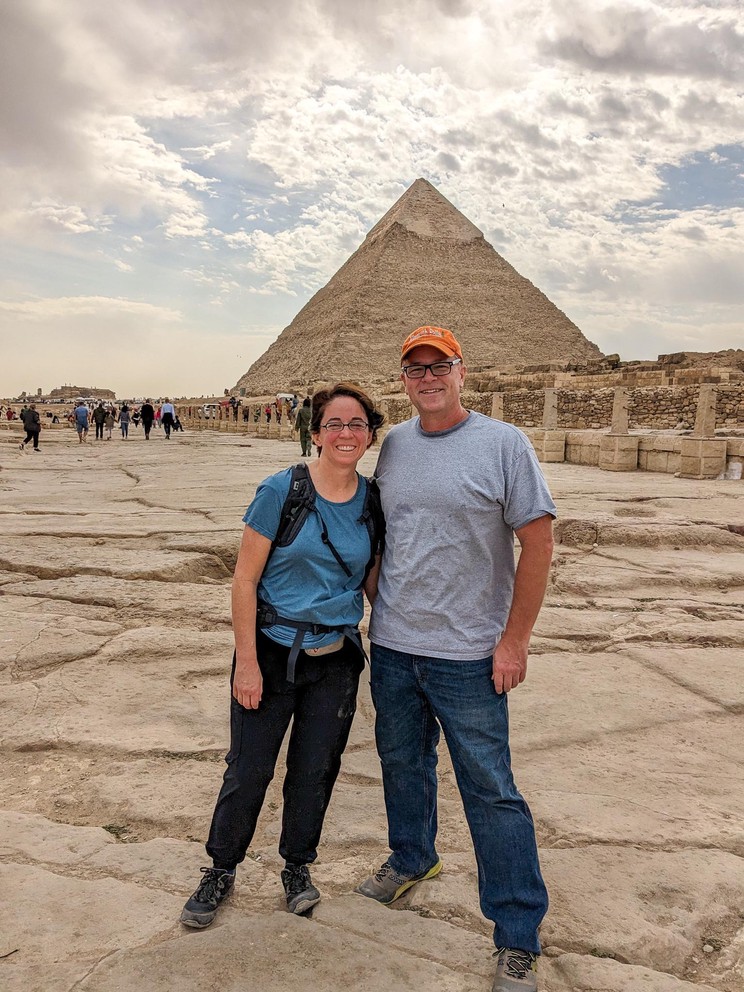 a man and woman stand in the Giza Necropolis with the Pyramid of Khafre in the background