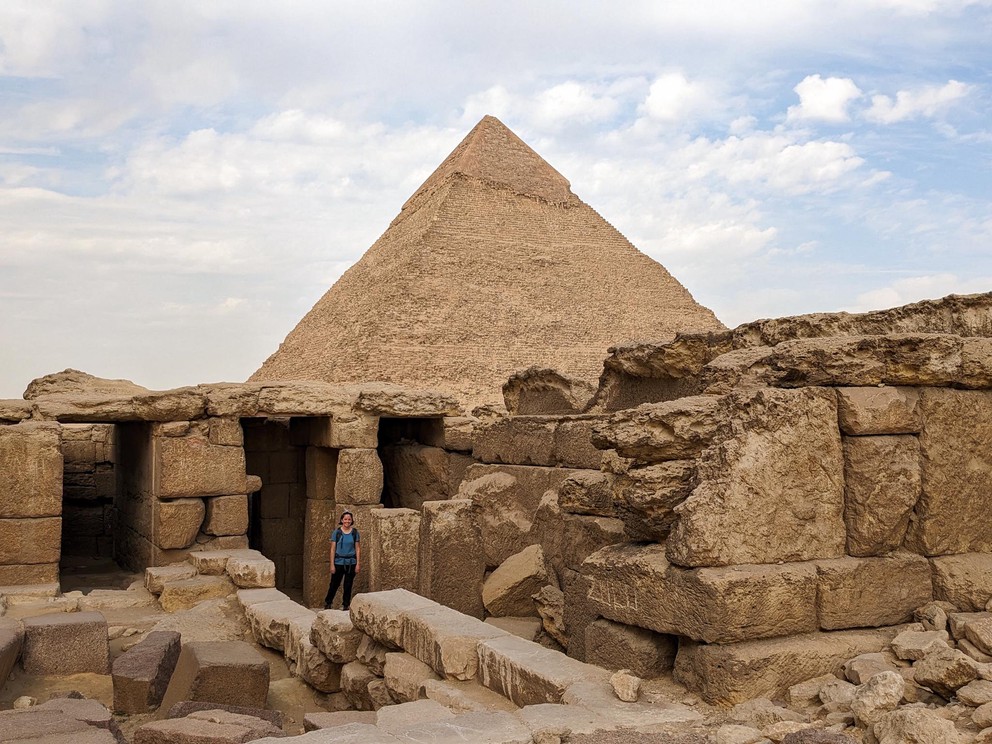 a woman explores some ruins in the Giza Necropolis with the Pyramid of Khafre in the background