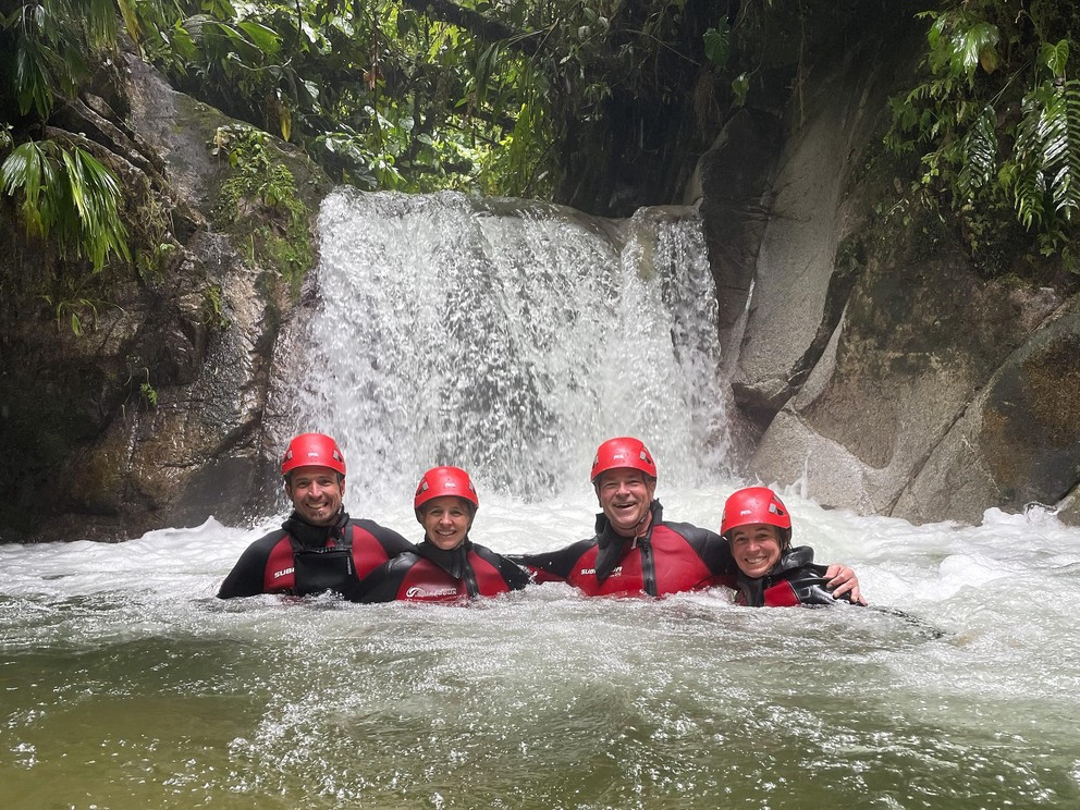 four tourists enjoy standing in a river below a waterfall