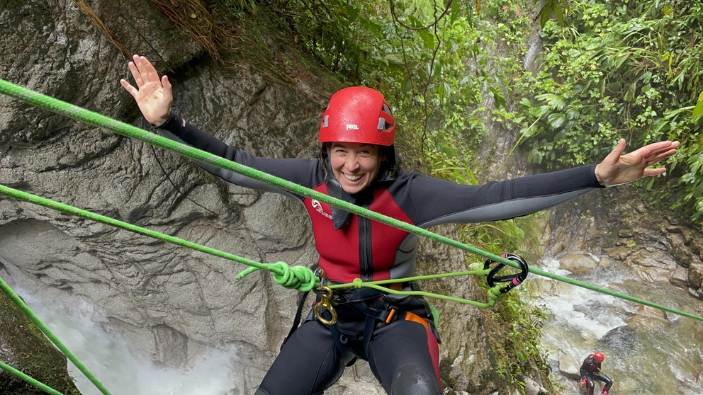 a smiling woman prepares to ride a makeshift zipline down a waterfall