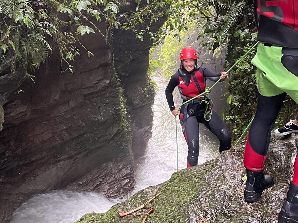 a smiling woman prepares to rappel into a tropical waterfall