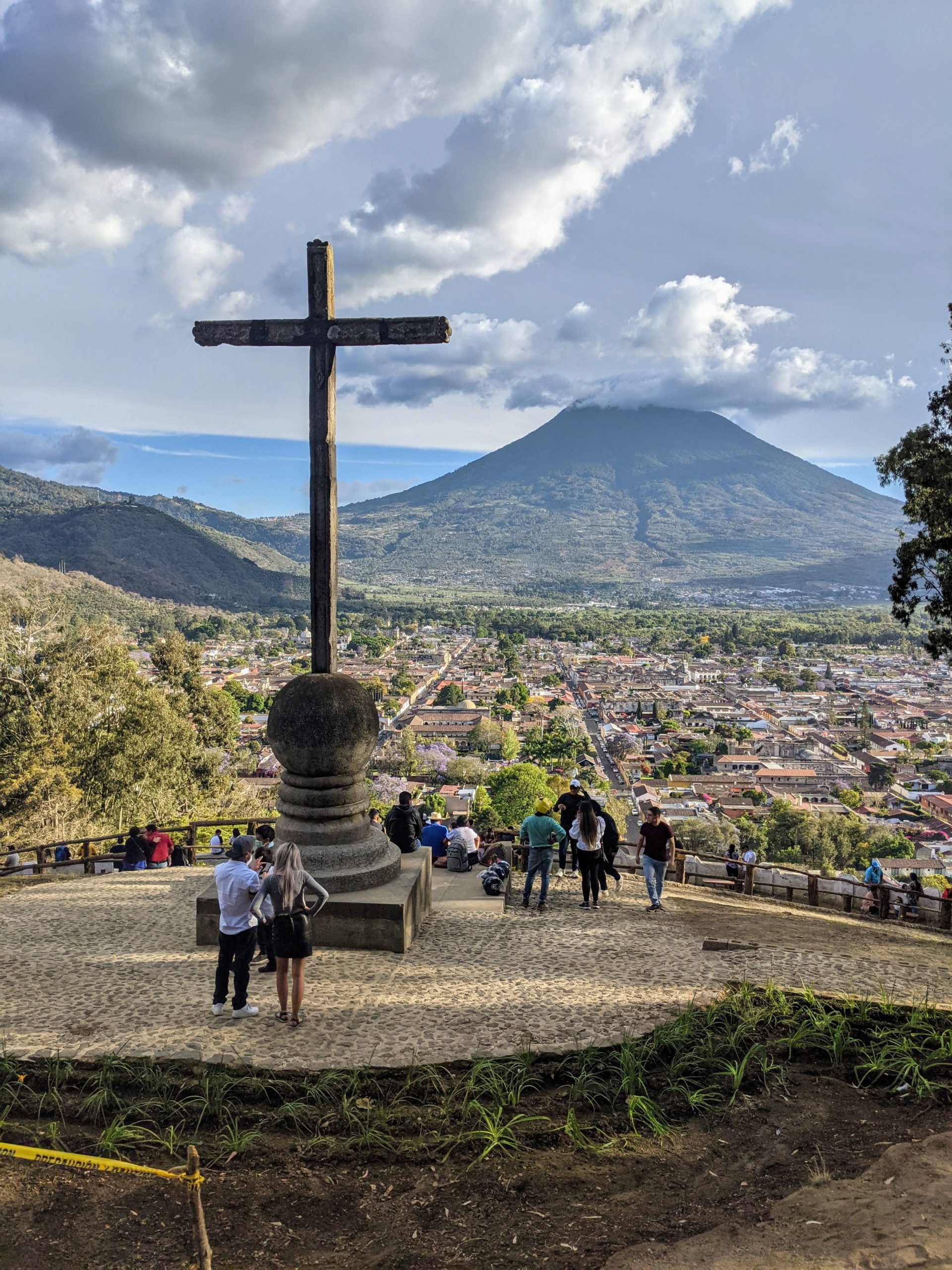 a large cross sits on a hillside overlooking Antigua, Guatemala and the Agua Volcano