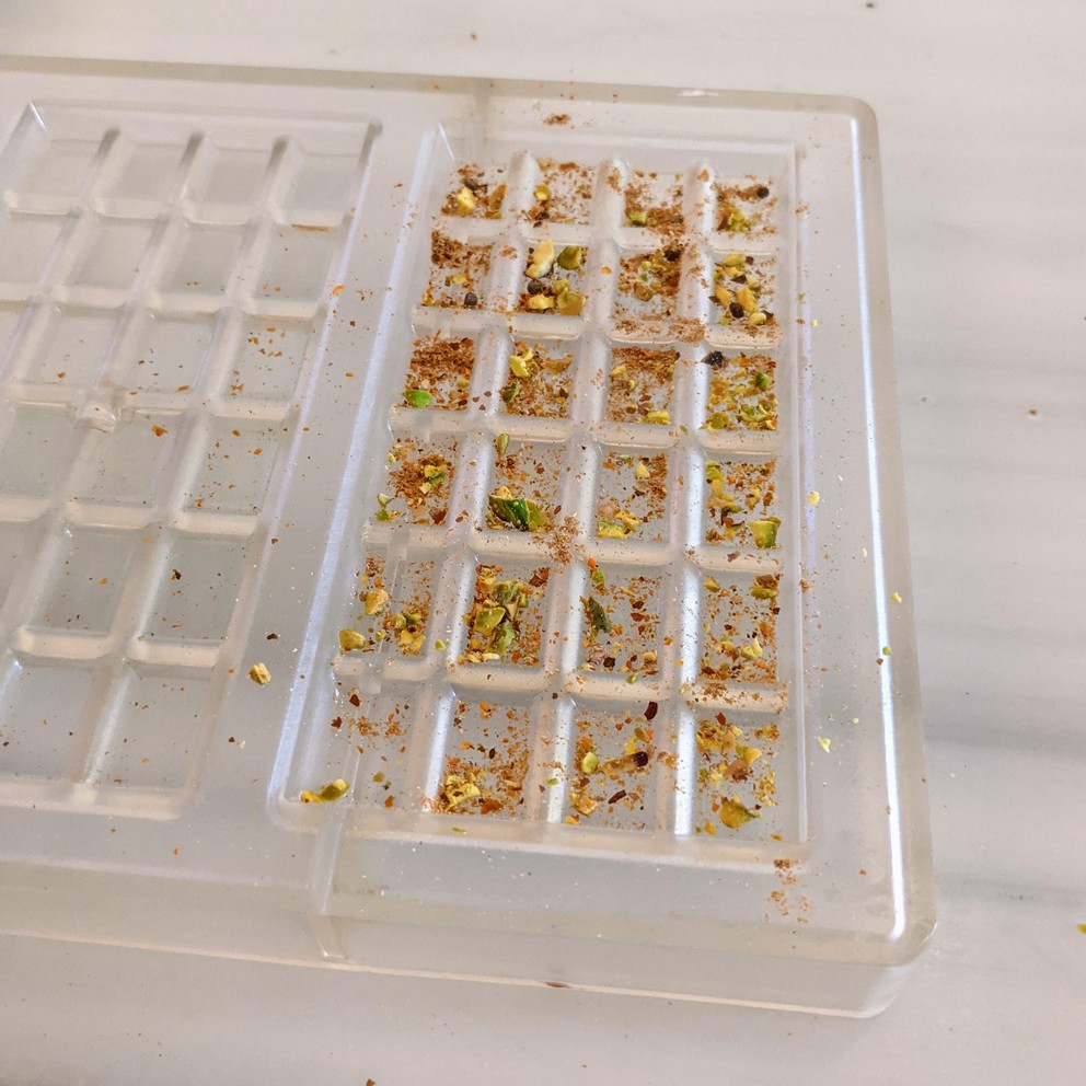 ground spices have been placed in each cell of a plastic mold so they can be included in the chocolate bar when the liquid chocolate is poured over them
