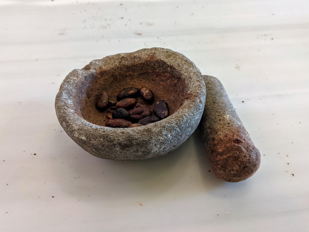 a mortar and pestle with a few roasted and shelled cacao beans ready to be ground into a paste