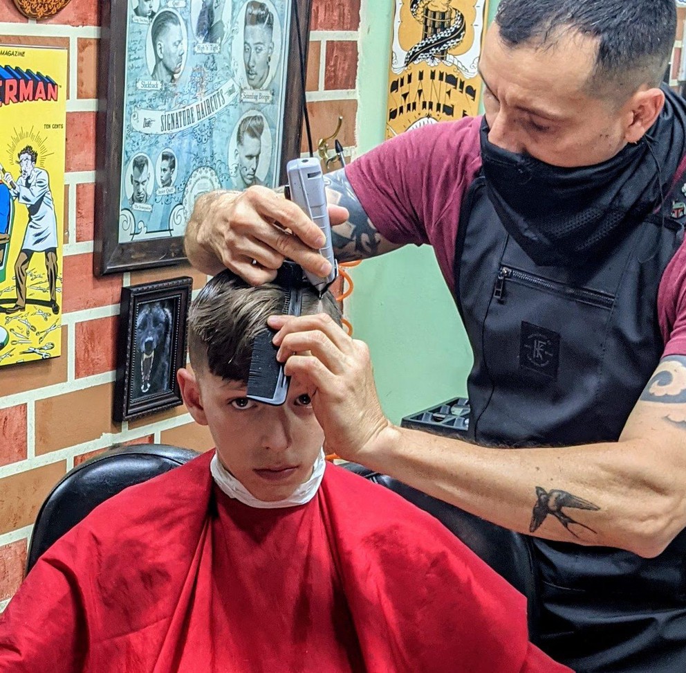 a barber uses his clippers to cut a hard part for a patron receiving a haircut