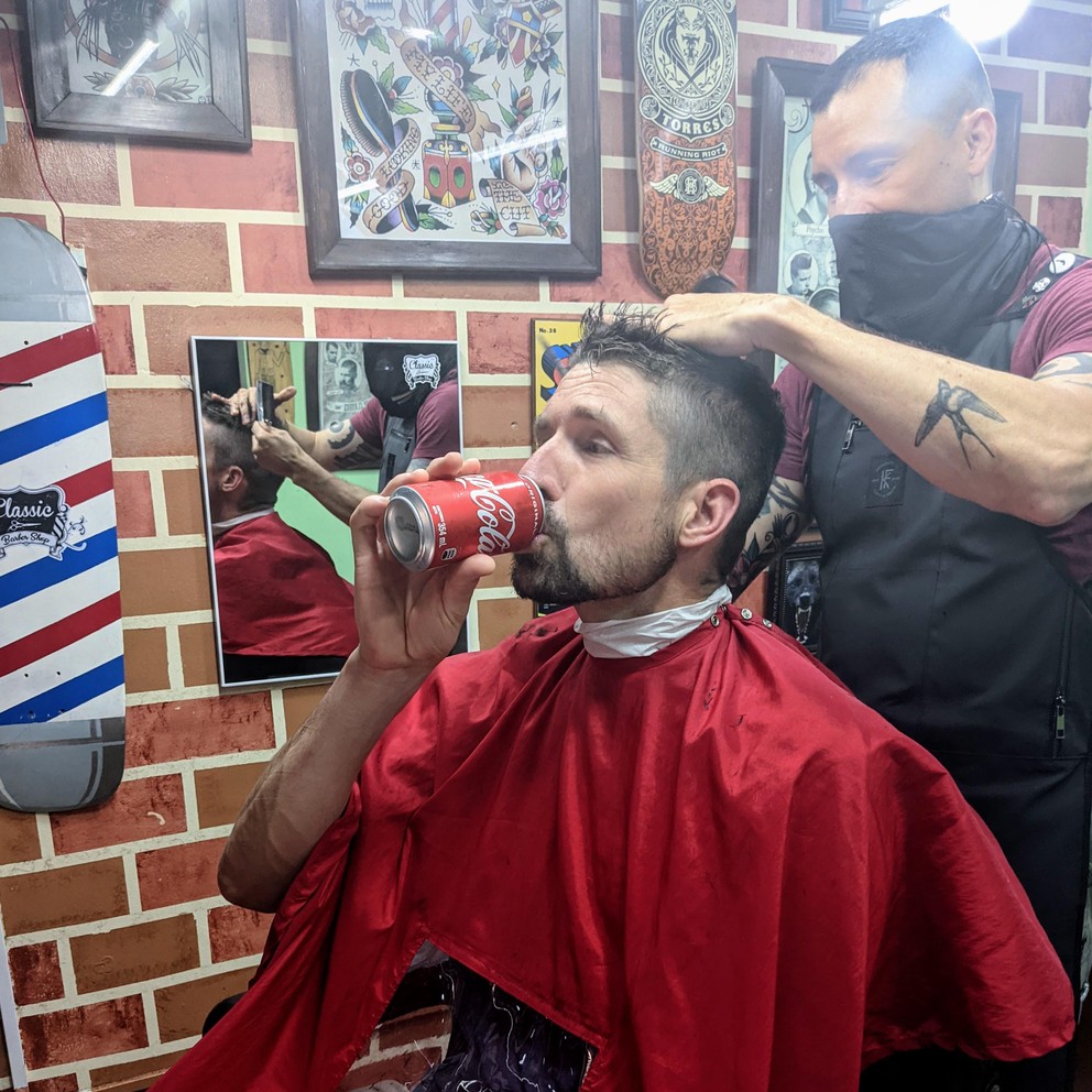 a customer drinks an ice-cold Coca Cola while receiving a haircut at the Classic Barber Shop in Antigua, Guatemala