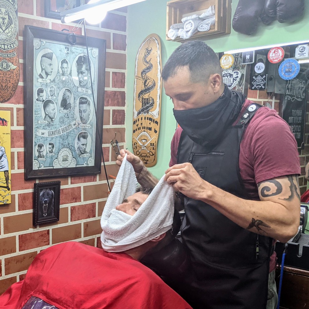 a hot towel is wrapped around the face of a customer to prepare his skin for a shave with a straight razor at the Classic Barber Shop in Antigua, Guatemala