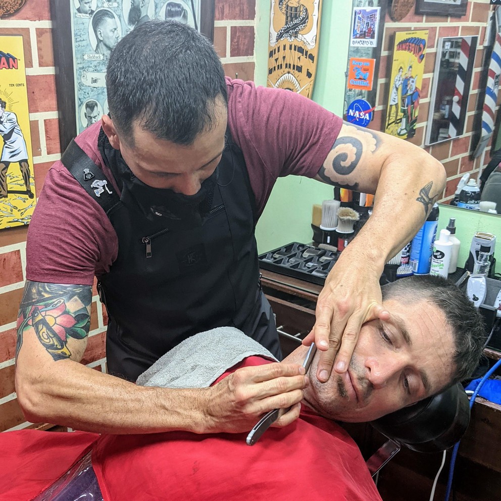 a barber uses a straight-edge razor to shave a customer at the Classic Barber Shop in Antigua, Guatemala