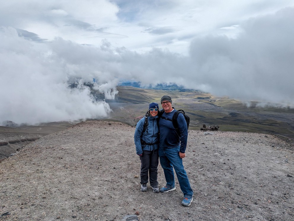 two people pose on a flat spot on the side of a high mountain