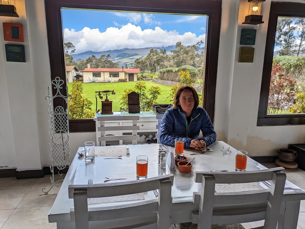 a woman sits in a restaurant at a table in front of a large window looking over the countryside