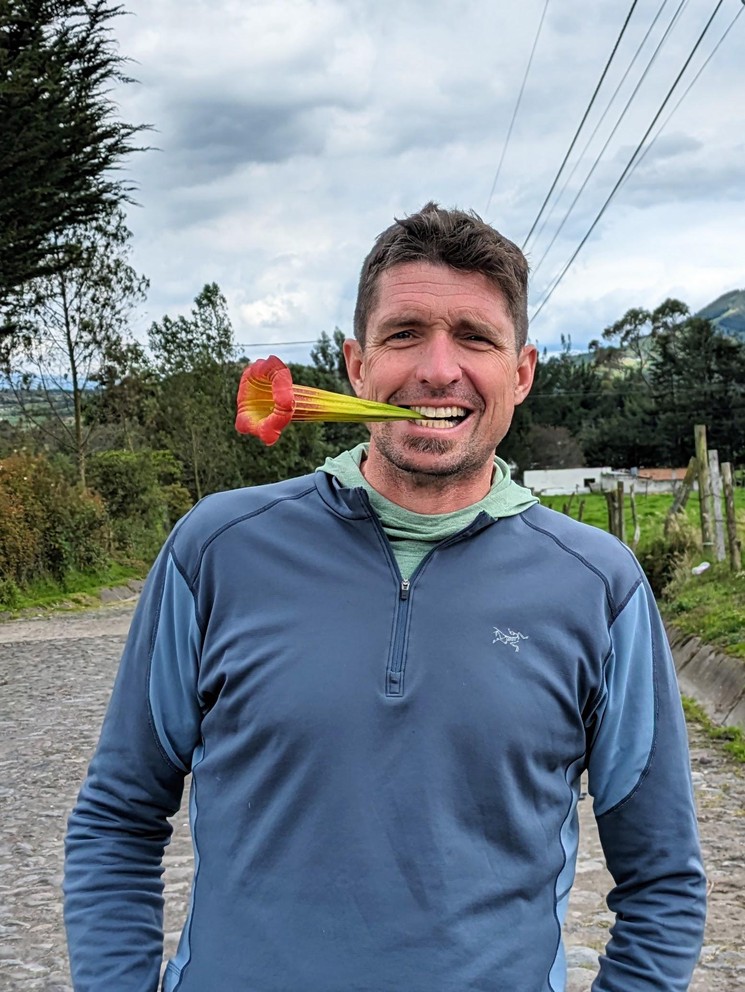 a man smiles with a flower from a red angel's trumpet in his mount
