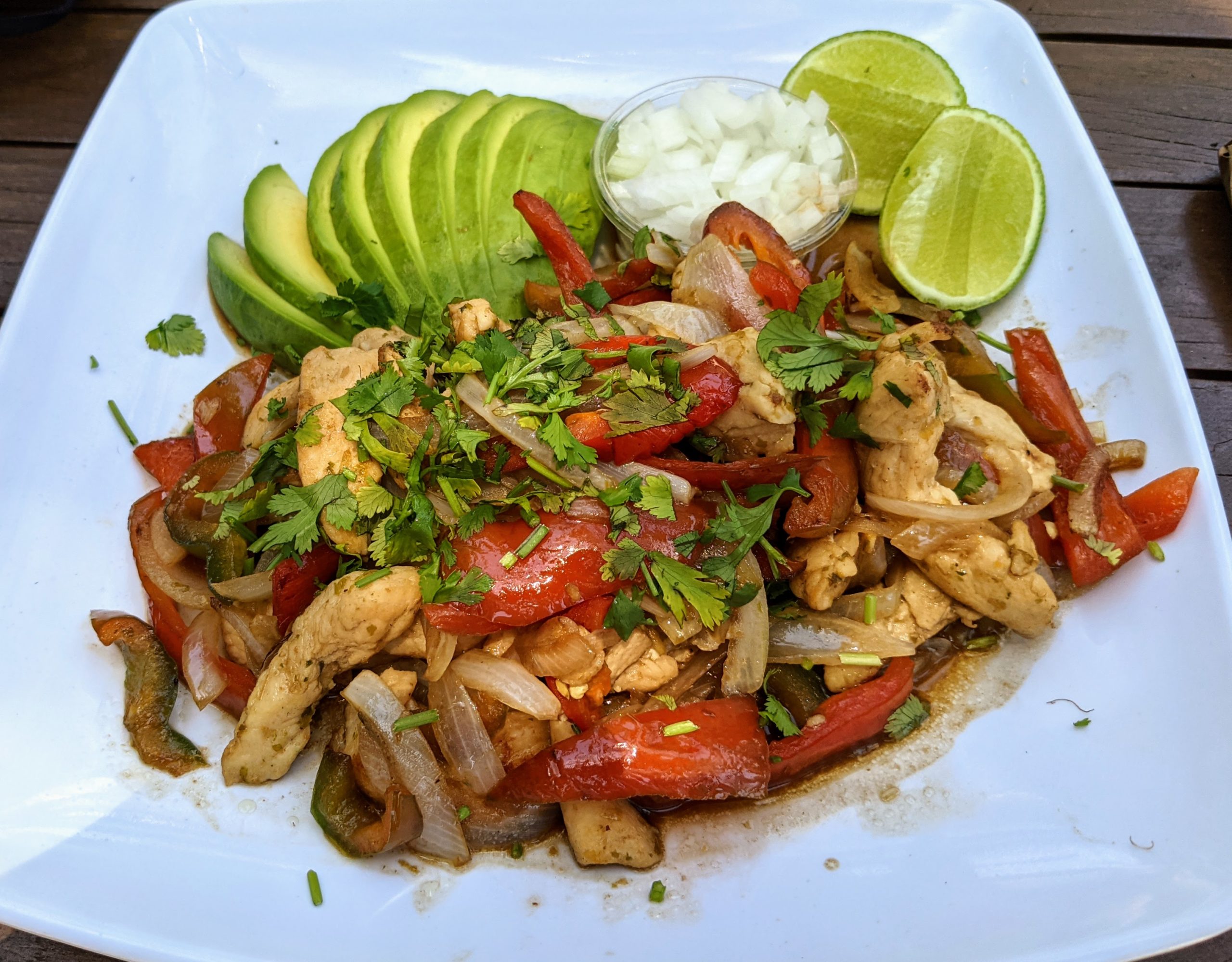 a white plate filled with grilled chicken, grilled vegetables, sliced avocado, onions, and limes