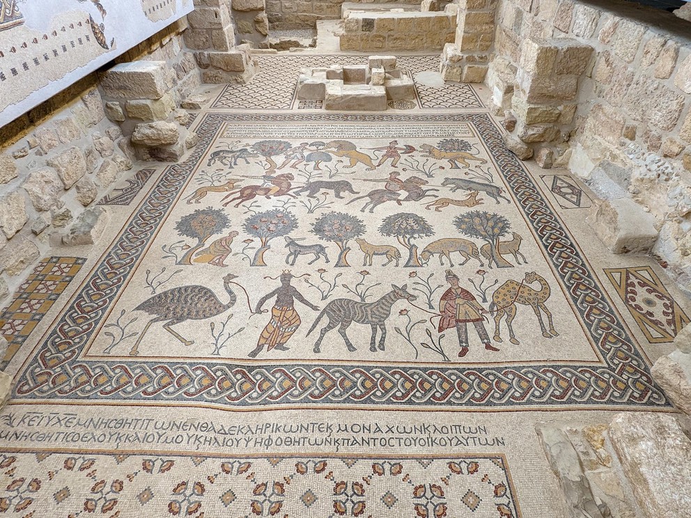 a mosaic tile floor depicting different types of men, animals, and trees with inscriptions in Greek