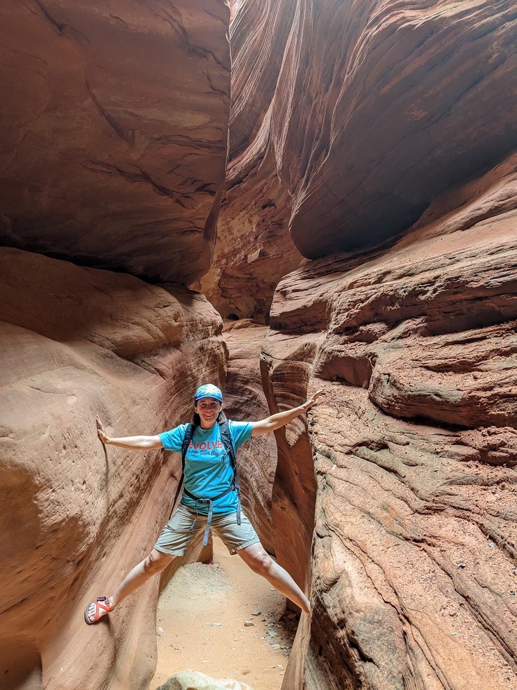 a woman stems between two walls of a narrow slot canyon