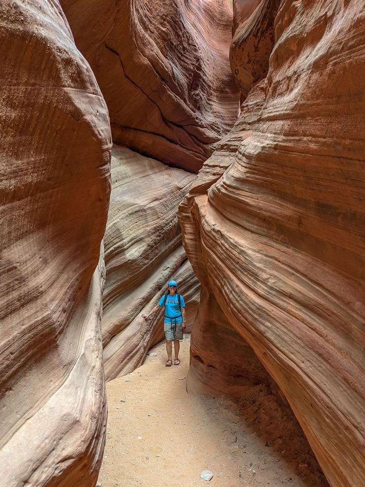 a woman walks down a light orange sandy slot canyon