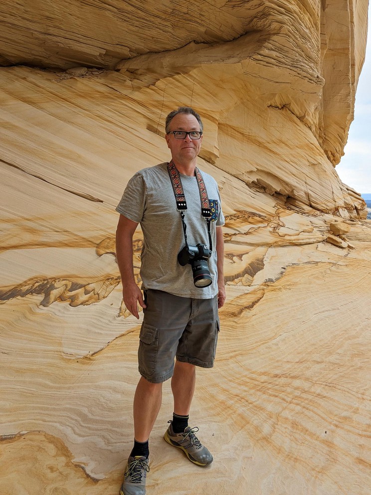 a man with a camera looks amazed at the yellow ice-cream colored sandstone formation that surrounds him