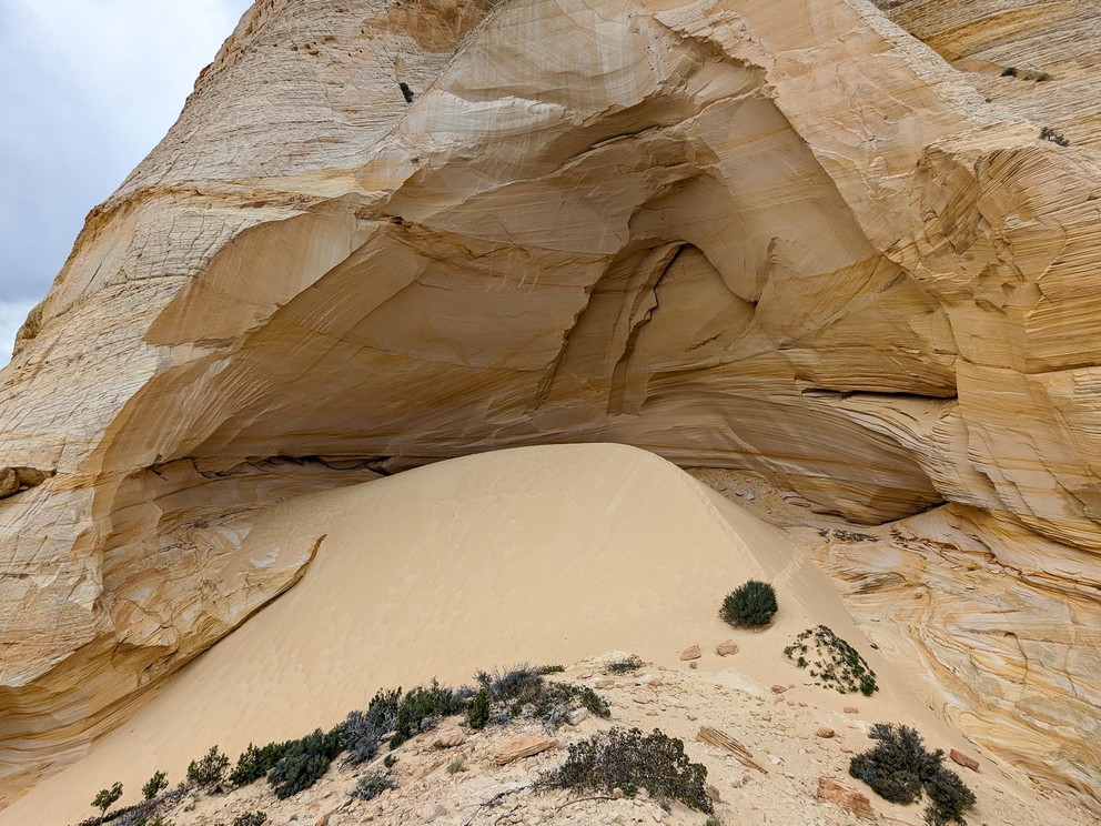 creamy soft yellow sand sits in a large pile inside a huge cut-out in a yellow and white sandstone formation