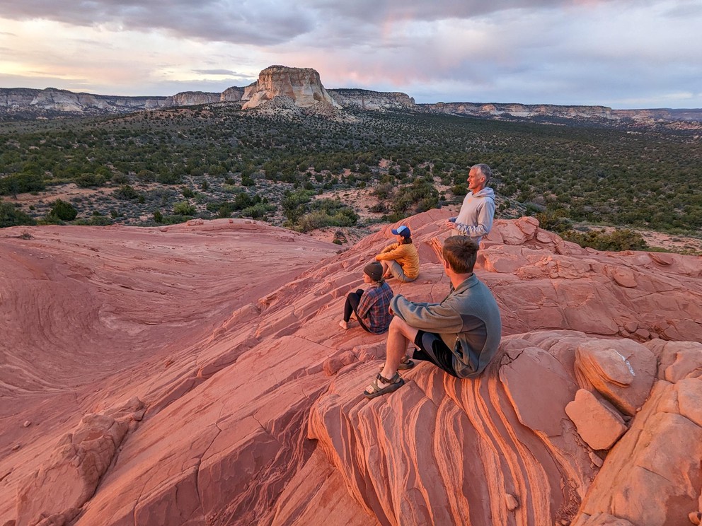 a group of campers enjoy a sunset from the top of a sandtone bluff