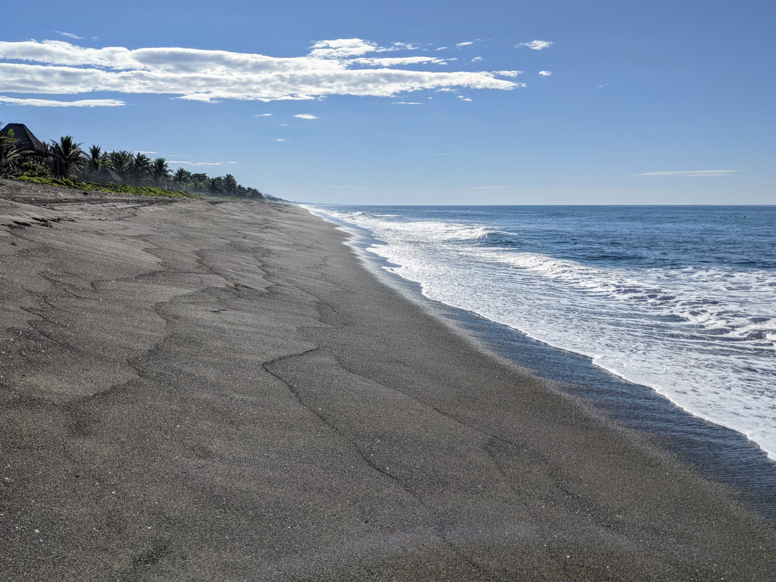 a steep black volcanic beach stretches far into the distance as the Pacific Ocean calmly laps up against its slope