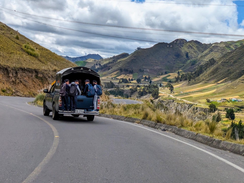 school children hang off the back of a pickup truck on their way to school