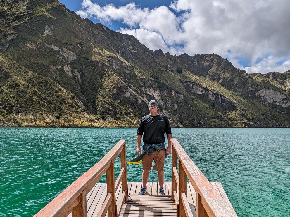 a man stands at the end of a wooden dock on a turquoise lake