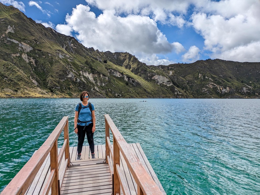 a woman stands at the end of a wooden dock on a turquoise lake