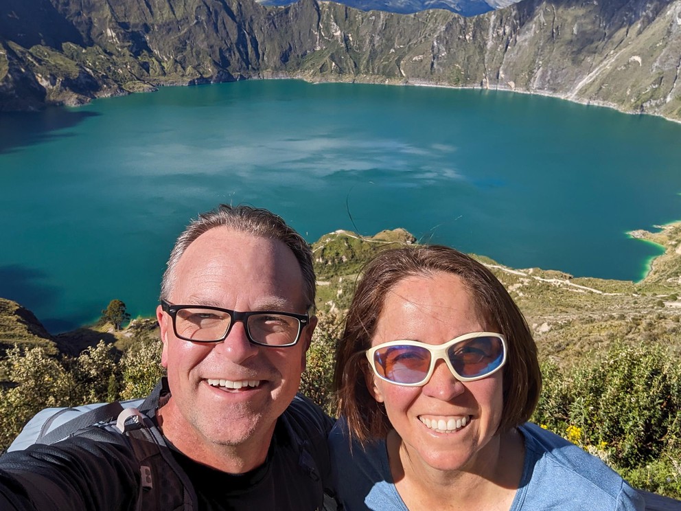 a man and woman take a selfie overlooking a wide emerald green volcanic lake