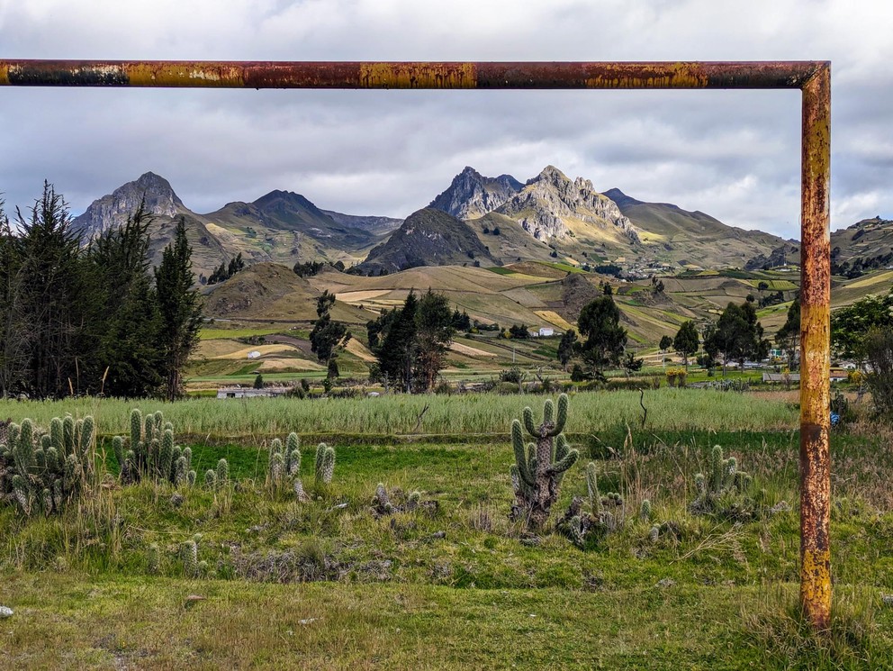 a rusty soccer goal post frames steep mountains and farmland behind it