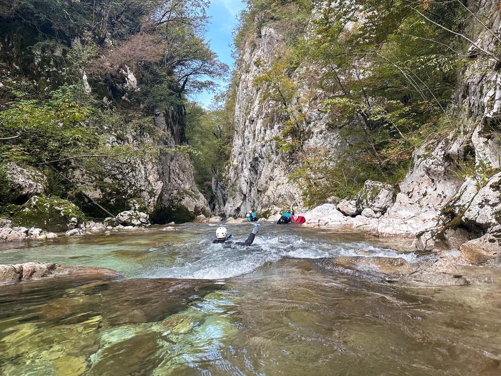 several adventurers float down a crystal clear river as it cuts through a narrow canyon