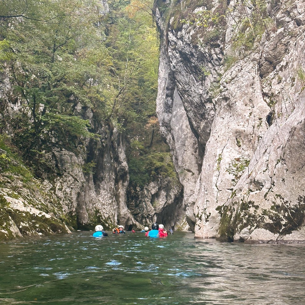 several adventurers float down a crystal clear river as it cuts through a narrow canyon