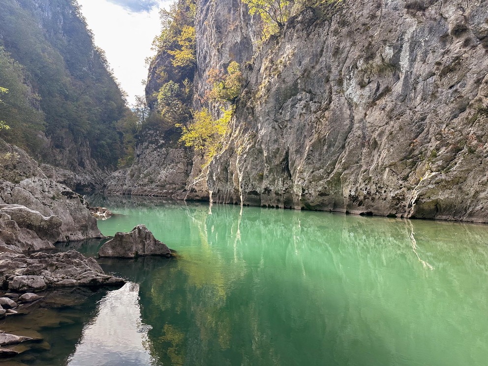 a deep emerald pool of water spans from edge to edge in a deep narrow canyon