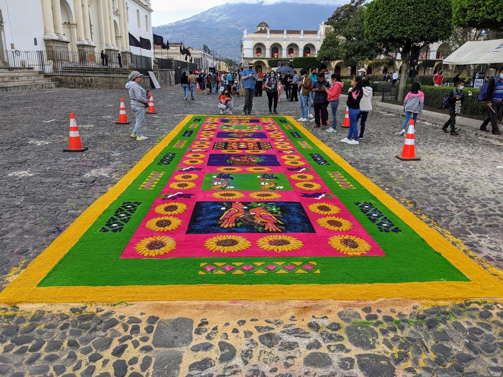 tourists and onlookers gather to enjoy the artistry of a carpet built for semana santa in downtown Antigua, Guatemala