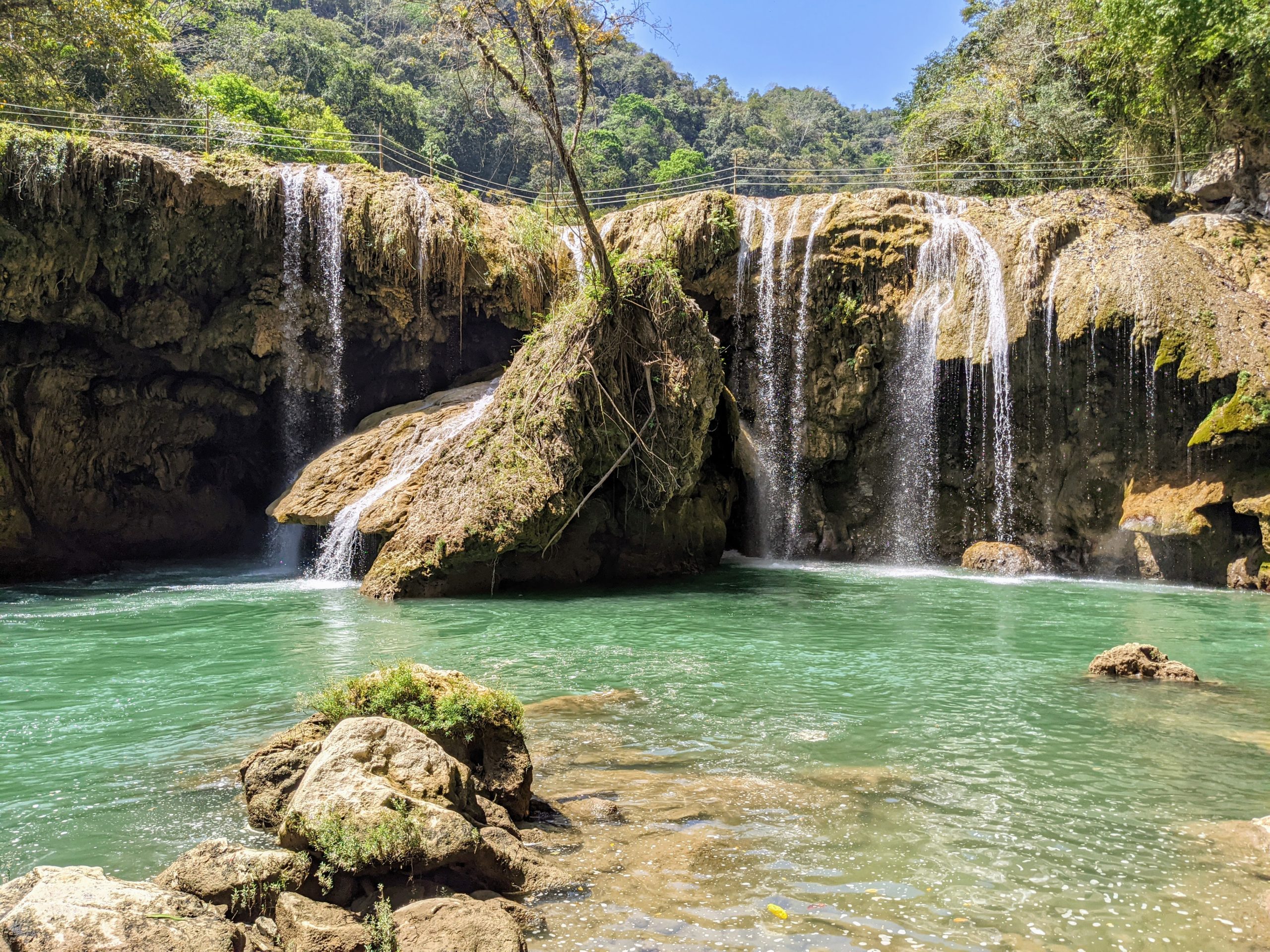 Water falls over yellow limestone cliffs into a turquoise river