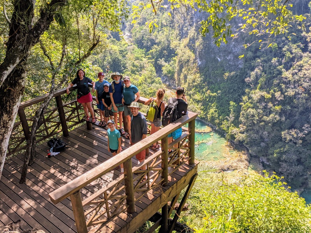 a group of tourists pose on a platform overhanging the turquoise pools of Semuc Champey