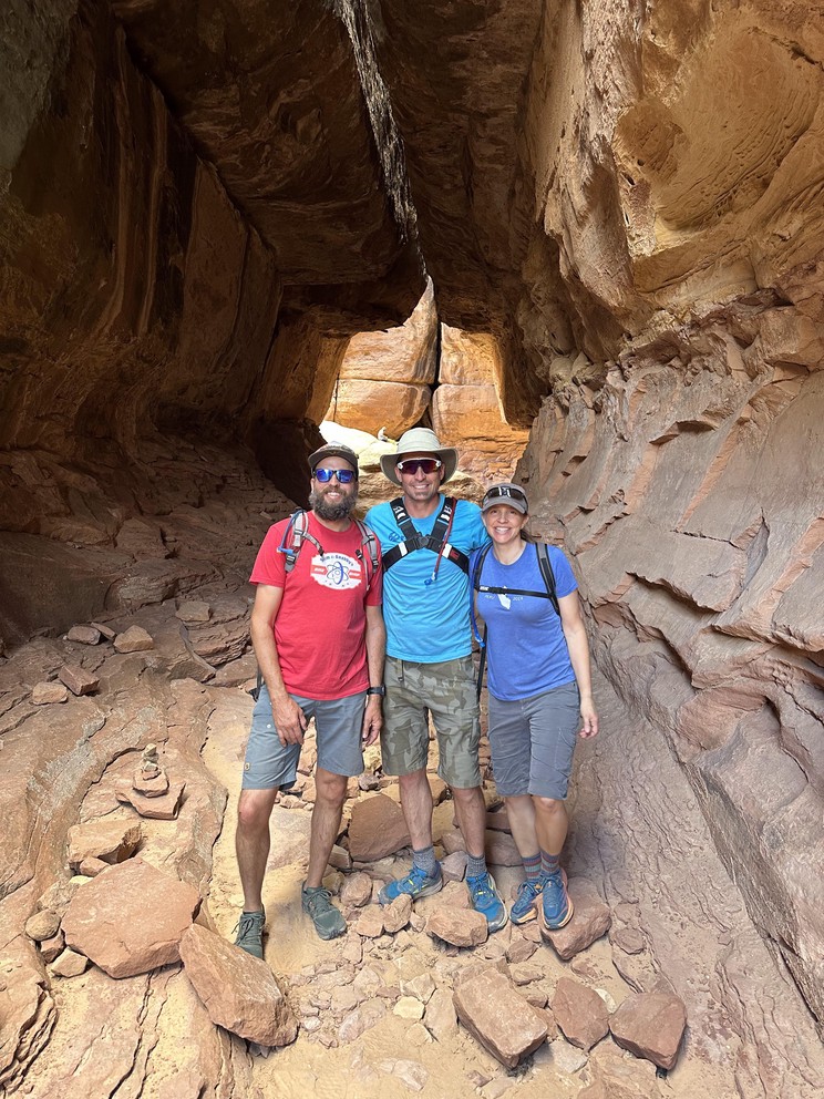 a group of hikers walk through a long narrow sandstone canyon that closes at the top