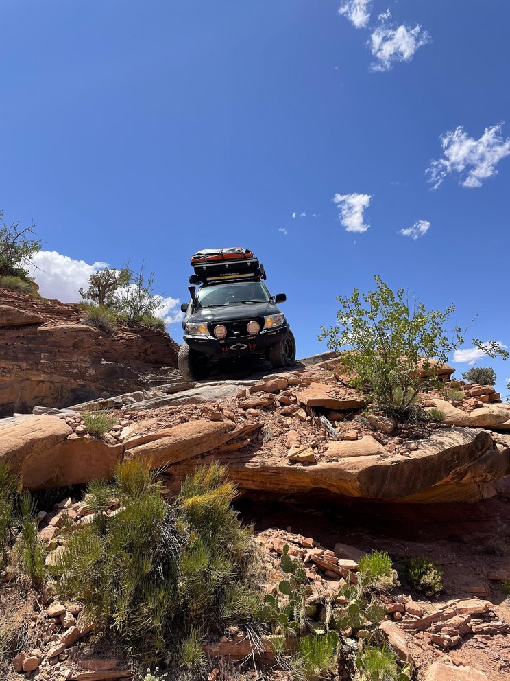 a modified Lexus GX470 descends a natural staircase of sand and rock with sandstone formations all around