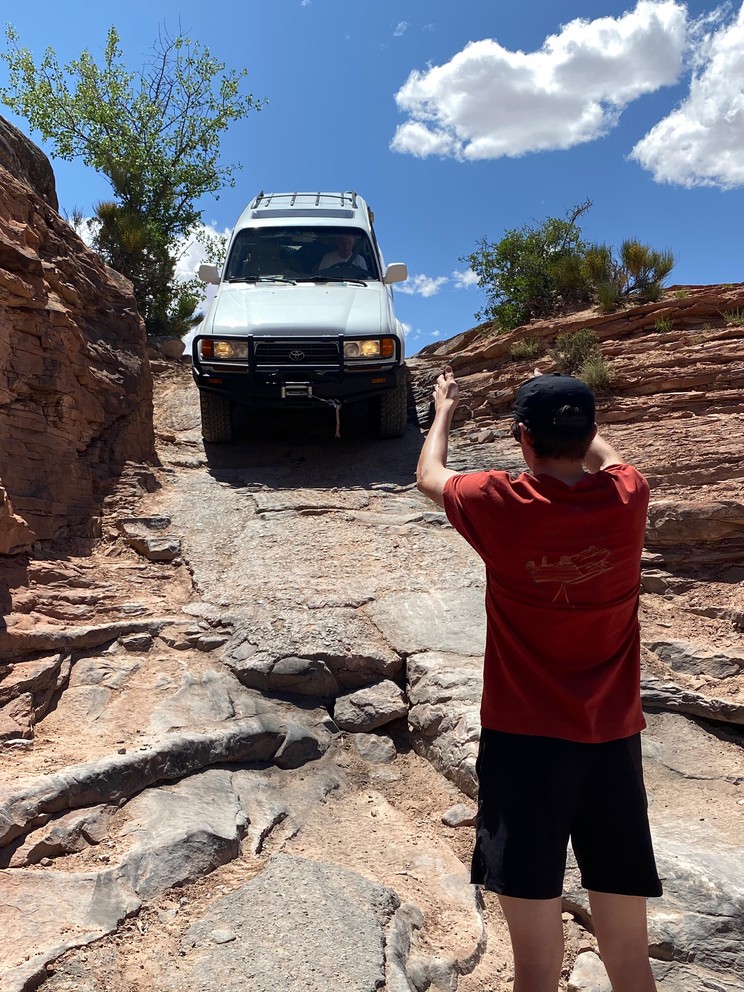 a Toyota Land Cruiser descends a natural staircase of sand and rock with sandstone formations all around