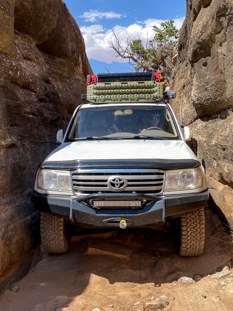 a young driver navigates a white Toyota Land Cruiser through a narrow sandstone squeeze