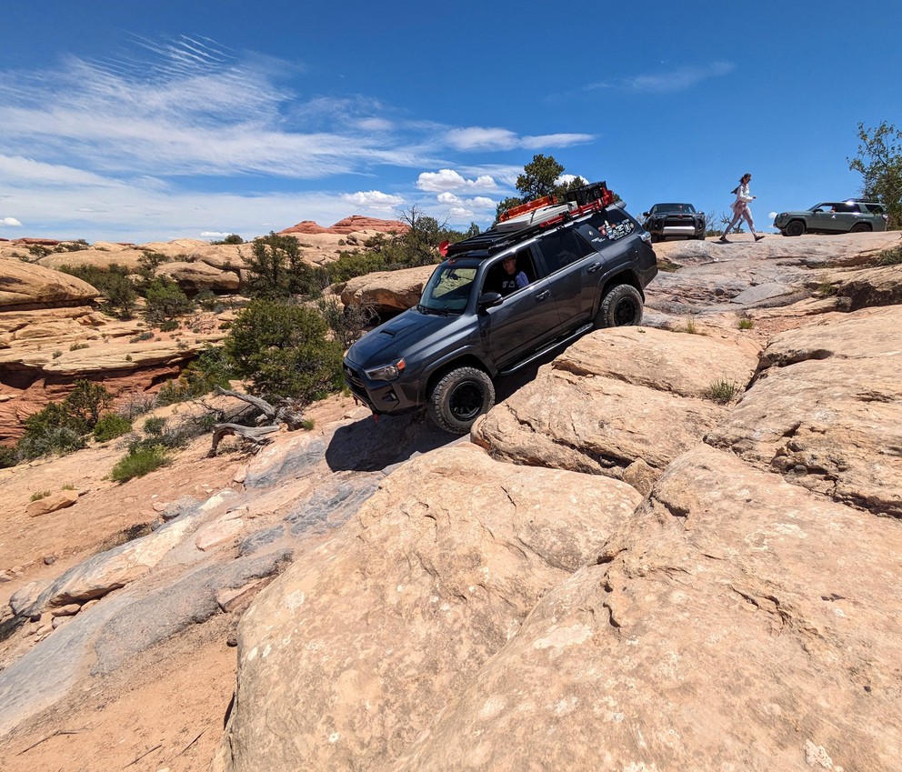 a Toyota 4Runner descends a natural staircase of sand and rock with sandstone formations all around