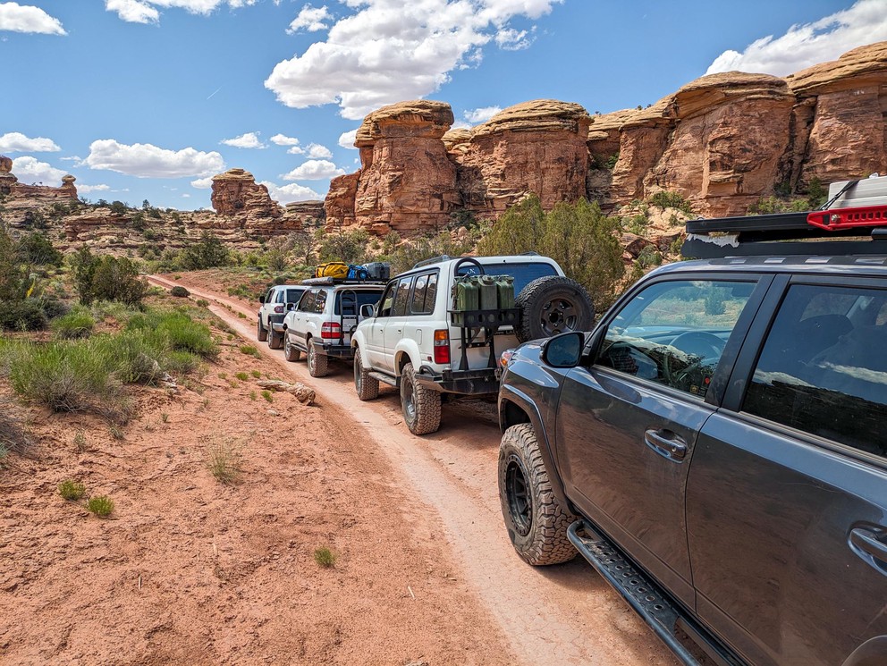 several Toyota SUVs lined up on a dirt road with sandstone formations all around