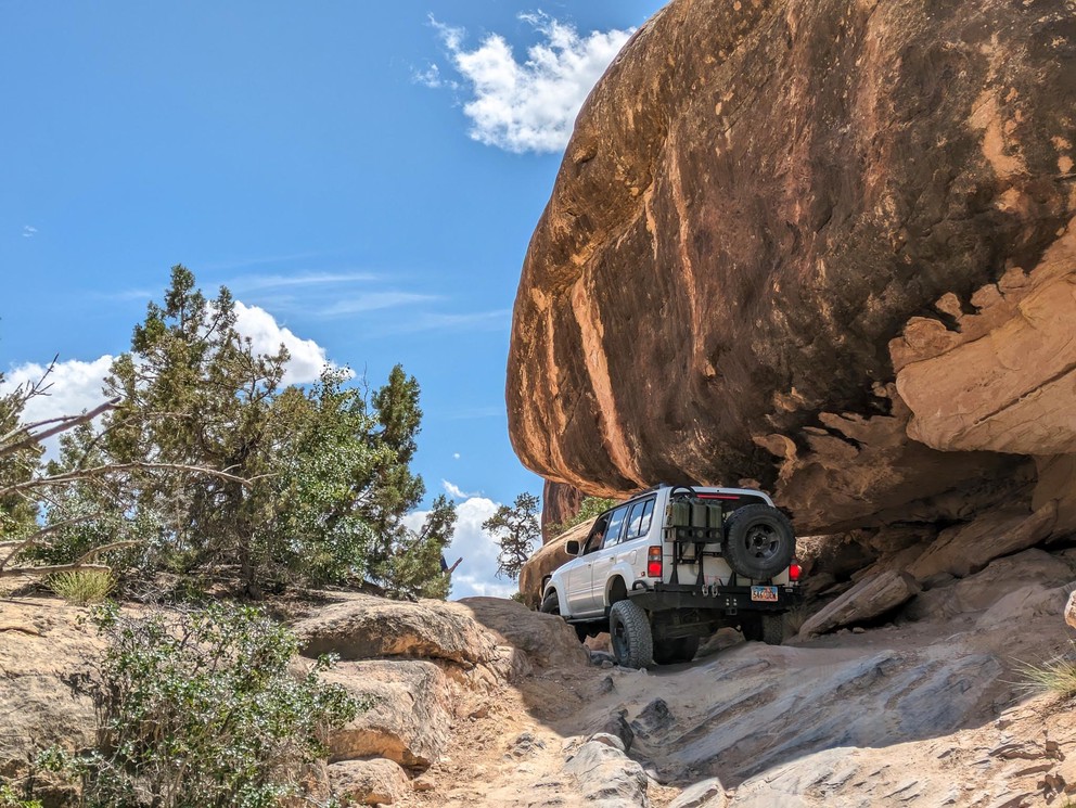 a Toyota Land Cruiser flexes its rear suspension as it drives under the overhanging part of a huge sandstone formation