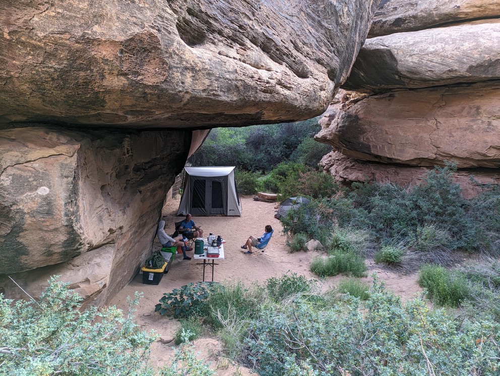 campers and a tent setup for the night under the overhang of a huge boulder