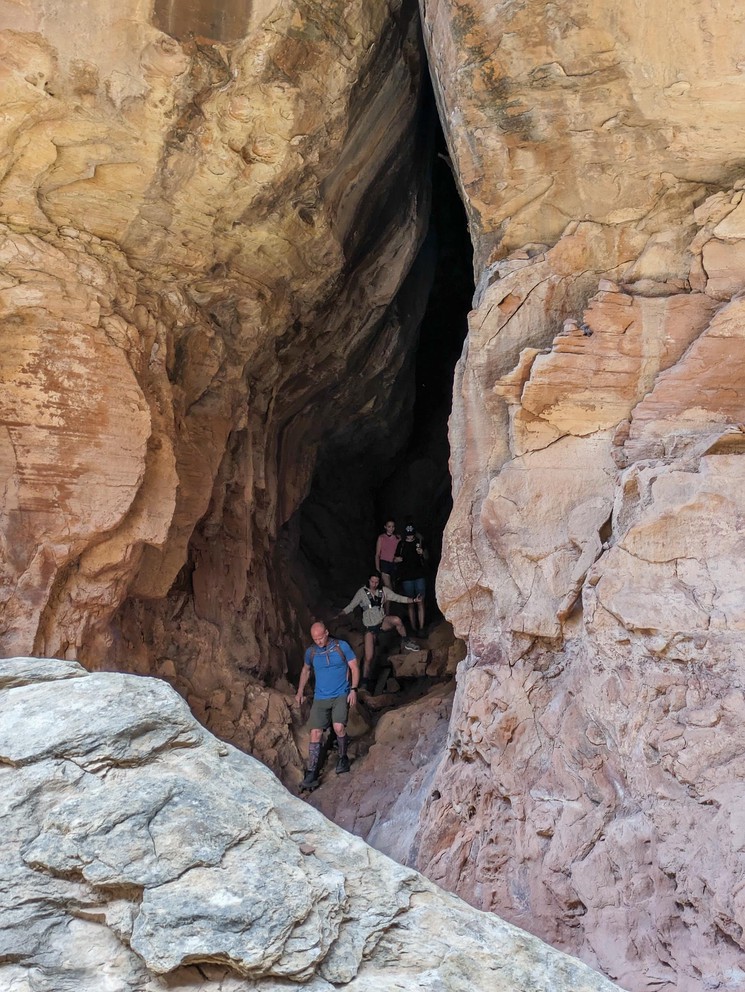 a group of hikers walk through a long narrow sandstone canyon that closes at the top