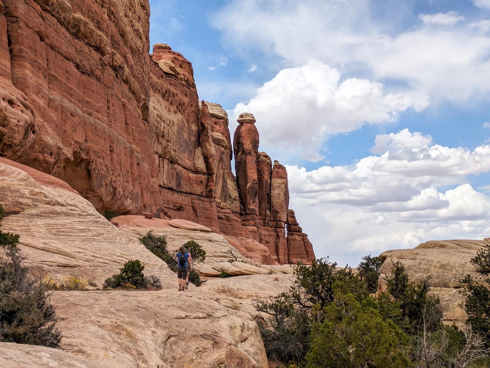 hikers walk along a lip next to sandstone cliffs towering over them