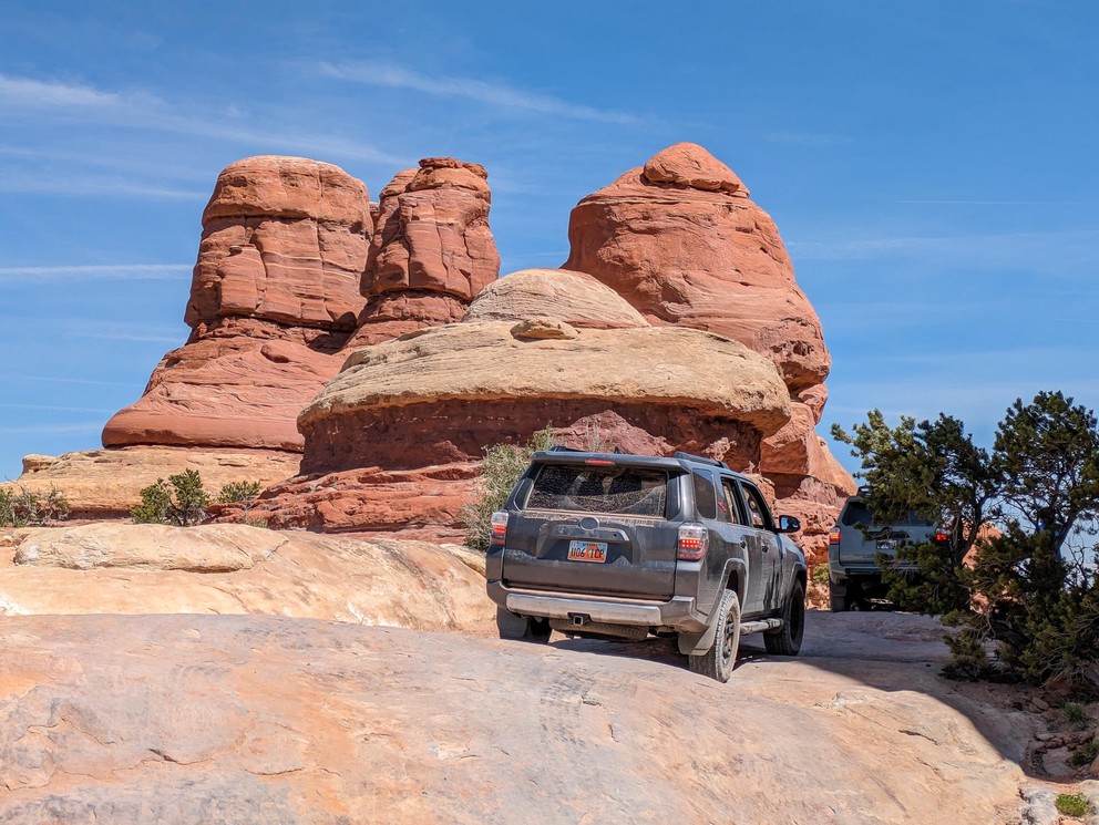 two Toyota 4Runner SUVs drive over large rocks next to some brigt orange sandstone formations